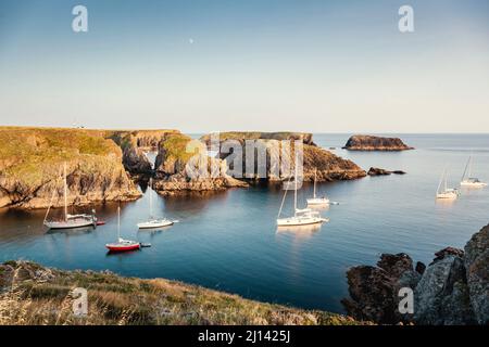 Die ruhigen Buchten an der felsigen Küste der Insel Belle Ile en Mer bieten einen geschützten Ankerplatz für viele Segelboote im ruhigen Sonnenuntergang. Stockfoto