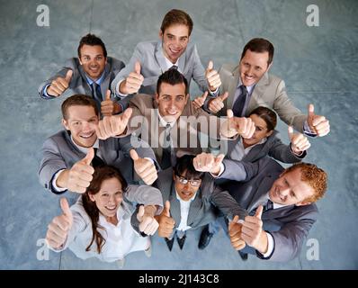 Nachdrückliche Zustimmung. Draufsicht auf ein erfolgreiches Geschäftsteam, das Ihnen mit Nachdruck Daumen nach oben zeigt. Stockfoto