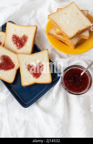 Toast, auf dem das Herz aus Marmelade besteht. Überraschungsfrühstück im Bett. Romantik zum Valentinstag Stockfoto