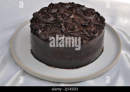 Nahaufnahme von hausgemachtem Schokoladenkuchen auf weißem Gericht, auf dem weißen Tisch Stockfoto