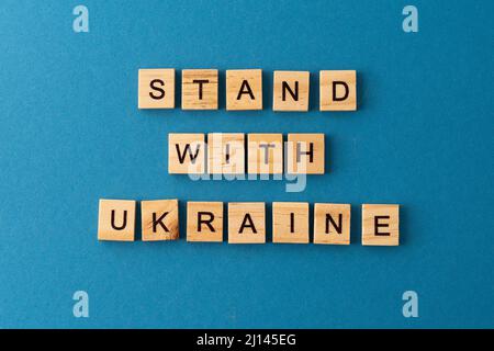 Stand mit Ukraine Hintergrund. Satz aus Holzbuchstaben. Unterstützt das ukrainische Volk. Krieg beenden. Wörter aus der Draufsicht. Die Sätze sind in Holzbuchstaben ausgelegt. Motivation. Stockfoto