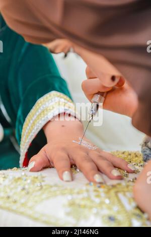 Künstlerin, die Henna-Tätowierung auf Frauenhänden anwendet. Mehndi ist traditionelle marokkanische Dekorationskunst. Nahaufnahme, Draufsicht Stockfoto