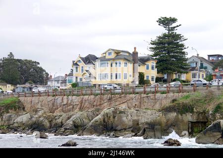 Meereswellen brechen an felsiger Küste entlang des Ocean View Blvd in Pacific Grove, Kalifornien. Malerisch mit Verkehr, Joggern und Fußgängern auf einem stürmischen Stockfoto