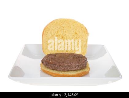 Einfacher Hamburger auf einem Eierbrotbrötchen auf quadratischem weißem Porzellanteller, isoliert auf Weiß. Bereit für die Zugabe von Gewürzen. Stockfoto