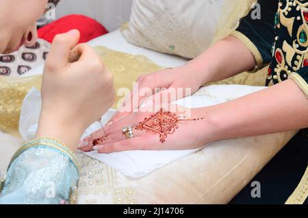 Künstlerin, die Henna-Tätowierung auf Frauenhänden anwendet. Mehndi ist traditionelle marokkanische Dekorationskunst. Nahaufnahme, Draufsicht Stockfoto