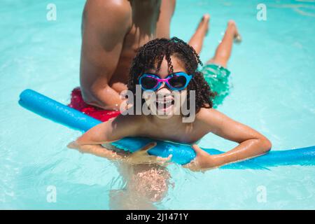 Hispanic Mann hilft Sohn schwimmen mit Schwimmer im Pool an sonnigen Tag Stockfoto