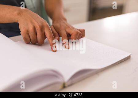 Verkürzte Hände eines blinden hispanischen Mannes, der zu Hause die Blindenschrift auf dem Buch berührt Stockfoto