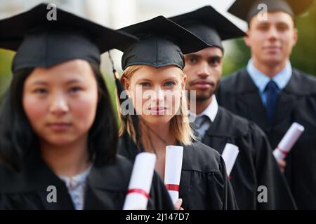Dies ist der Anfang, von allem, was Sie wollen. Eine Gruppe von Hochschulabsolventen, die in Mütze und Kleid stehen und ihre Diplome halten. Stockfoto