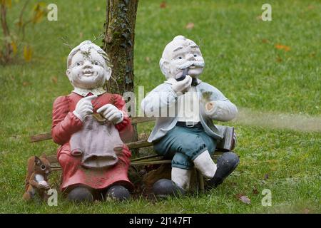 Figuren eines älteren Paares, das auf einer Bank in einem Garten sitzt, sich ausruhte und den Ruhestand genoss Stockfoto