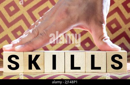 Ein Mann legt Holzblöcke mit dem Wort Fähigkeiten. Wissen und Fähigkeiten. Selbstverbesserung. Bildung Konzept. Ausbildung. Führungsqualitäten. Menschliche Fähigkeiten Stockfoto