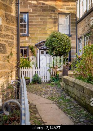 Traditionelles Steinhaus mit weißem Pfostenzaun, gelegen in einer schmalen Gasse in der Altstadt von Robin Hoods Bay, North Yorkshire. Stockfoto