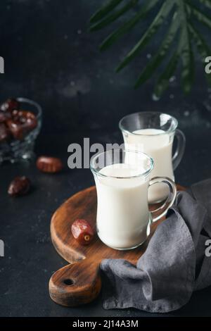 Ramadan Kareem Essen und Getränke. Teller mit Datteln, Glas Milch und Dattelpalmzweig auf schwarzem Hintergrund. Gerechter Muslimischer Lebensstil. Vegetarische Gerichte. S Stockfoto