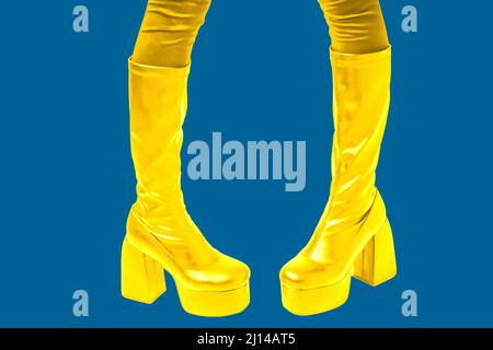 Damenfüße in goldenen Stiefeln mit hohen Sohlen auf blauem Hintergrund. Werbefoto von modischen Schuhen. Modische Kollektion von Schuhen mit hohem Absatz für Damen. Stockfoto
