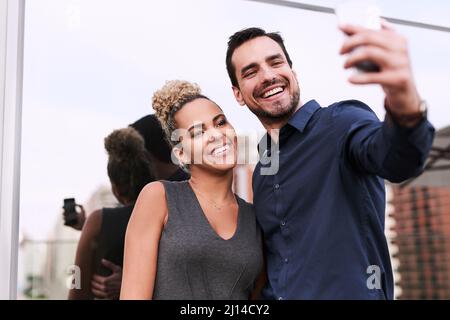 Welt, werden Sie bald unseren Erfolg sehen. Aufnahme von zwei Kollegen, die vor einem Büro zusammen ein Selfie machen. Stockfoto