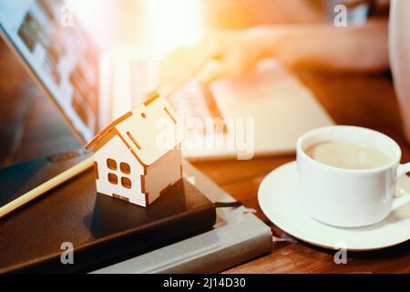 Modell des Holzhauses auf dem Hintergrund des Laptops. Konzept der Immobiliensuche im Internet. Kauf oder Versicherung von Wohnraum. Hintergrund. Stockfoto