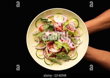 Direkt über der Ansicht eines beschnittenen, händhaltenden Tellers mit frischem Salat auf weißem Hintergrund Stockfoto