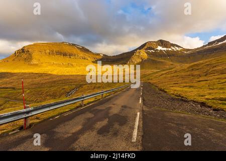 Sonnenuntergang über den Färöern, einem vulkanischen Archipel im Atlantischen Ozean. Die Straße zwischen den Hügeln. Eysturoy Island, Färöer-Inseln. Stockfoto