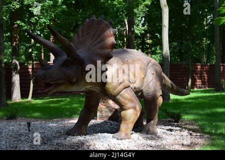 DINO PARK, KHARKOV - 8. AUGUST 2021: Dino Park Triceratops an einem sonnigen Tag spaziert ein riesiger Dinosaurier aus der Jurassischen Zeit im Sommer durch den Wald. Eine wilde Eidechse g Stockfoto