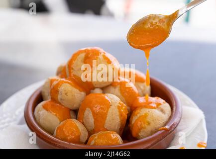 Löffel gießt würzige Mojo-Sauce auf Papas arrugadas in Tonplatte. Traditionelle Knitterkartoffeln von der Insel Gran Canaria, Spanien Stockfoto