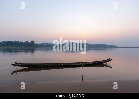 Ein traditionelles Holzboot auf dem Mekong Riverbank bei Sonnenaufgang, Spiegelung des Sonnenhimmels auf dem Fluss. Grenze zwischen Thailand und Laos. Weicher Fokus auf dem Boot. Stockfoto