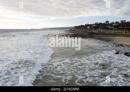 Meereswellen am bewölkten Tag in Meloneras, Gran Canaria. Touristen auf Strandpromenade auf den Kanarischen Inseln, Spanien Stockfoto