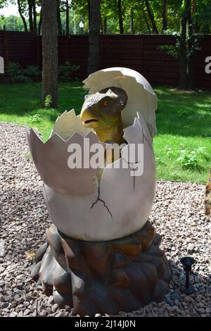 DINO PARK, KHARKOV - 8. AUGUST 2021: Dinosaurier-Statue im Waldpark in der Natur als Hintergrund. Ein kleiner Dinosaurier schlüpft aus einem Ei. Das prähistorische Stockfoto