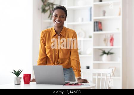 Positive kurzhaarige afroamerikanische Frau, die im Büro posiert Stockfoto
