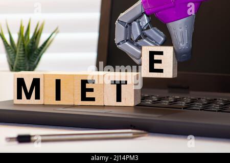 Konzept für die Vermietung eines Hauses. Ein Modellhaus, das auf einer Wiese steht. Würfel bilden das deutsche Wort Miete RENT auf Englisch. Stockfoto