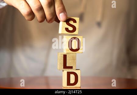 Der Makler die Hand einen Würfel mit einem Bild des Hauses das Wort verkauft. Konzept der Verkauf eines Hauses, einer Wohnung, Immobilien Markt der Unbeweglichkeit. Tra Stockfoto