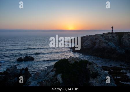 Sonnenuntergang über dem Atlantischen Ozean mit einem kleinen Leuchtturm mit Blick auf Praia Pequena an der Küste von Vicentine in der Nähe von Porto Covo, Alentejo - Portugal. Stockfoto