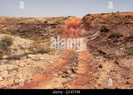 Eine Geländewagenstrecke schlittert durch die bunten Böden und Steine des großen Makhethesh Gadol-Krater Yeruham in Israel mit einem blauen Himmel in der BA Stockfoto