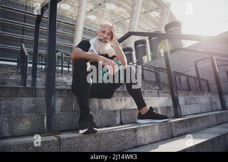 Porträt von attraktiven gesunden fröhlich Ruhestand grauhaarigen Mann arbeiten Trinkwasser sitzen auf Steintreppen aktives Leben im Freien Stockfoto