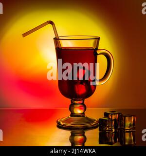 Kalter Tee, Cocktail, Fruchtgetränk in einer hohen Glasschale mit Trinkhalm auf einem Tisch mit Eisstücken. Rotes Getränk mit Eis in einem Becher auf einem schönen Br Stockfoto