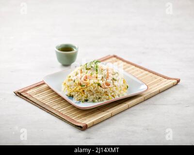 Gebratener Reis mit gewürfelten Garnelen mit Sauce isoliert auf Holzmatte Seitenansicht auf grauem Hintergrund ein Morgenmahl Stockfoto