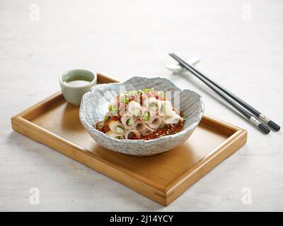 Pork Belly in Scheiben geschnitten mit würziger Knoblauchsoße mit Sauce, Essstäbchen auf einem Gericht isoliert auf Holzbrett Seitenansicht auf grauem Hintergrund Stockfoto