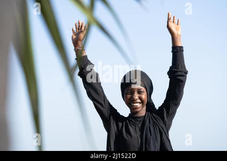 Afrikanische gebürtige schöne glückliche junge Frau mit erhobenen Armen, die sich für die Freiheit freut. Stockfoto