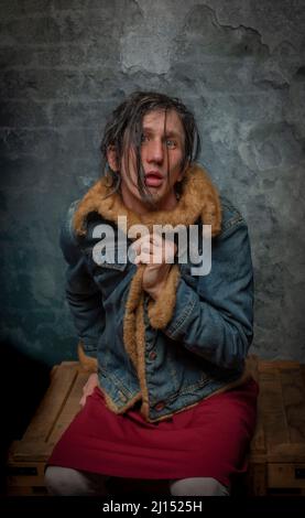 Schmutzige schwarze Haare verrückte Frau mit rotem Rock auf Holzkiste in der Nähe der alten Steinwand Stockfoto