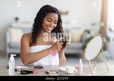 Hübsche afroamerikanische Dame, die sich um ihr lockiges Haar kümmert Stockfoto