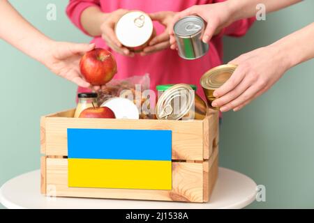 Menschen, die Spenden in einen Karton auf den Tisch legen. Humanitäre Hilfe für die Ukraine Stockfoto