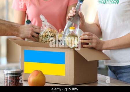 Freiwillige setzen Produkte in Box mit ukrainischer Flagge. Humanitäre Hilfe für die Ukraine Stockfoto