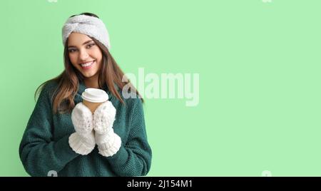 Junge Frau in warmen Handschuhen mit einer Tasse Kaffee auf grünem Hintergrund Stockfoto