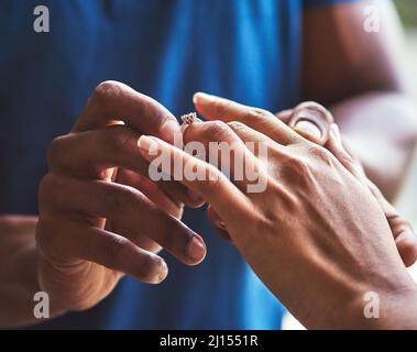 Es ist ein Fest der ewigen Liebe. Nahaufnahme eines nicht erkennbaren Mannes, der einen Verlobungsring auf den Finger seiner Verlobten legt. Stockfoto