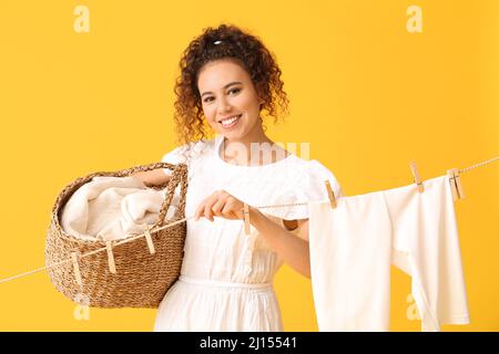 Junge afroamerikanische Frau mit Korb, hängender Wäsche und Wäscheklammern auf gelbem Hintergrund Stockfoto