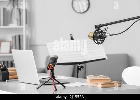 Moderner Arbeitsplatz mit Laptop, Büchern und Mikrofonen im Zimmer Stockfoto