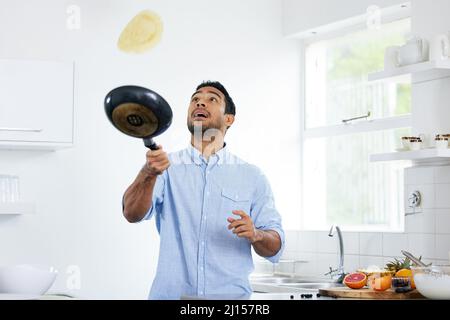 Du musst Spaß mit deinem Essen haben. Aufnahme eines jungen Mannes, der zu Hause Pfannkuchen zubereitet. Stockfoto