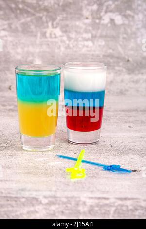 Zwei Cocktails in den Farben der russischen und ukrainischen Flaggen auf grauem Hintergrund Stockfoto