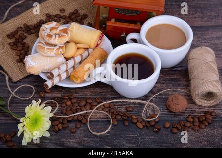 Zwei Tassen Kaffee, schwarz und mit Milch, Kaffeemühle, Kekse und Kaffeebohnen Stockfoto