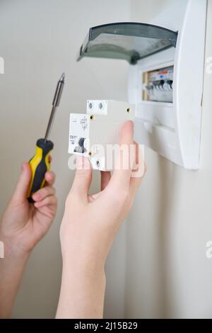 Eine Frau wechselt eine automatische Sicherung in einer Hauselektrik. Selbstreparatur und Austausch von elektrischen Geräten in der Wohnung, diy Stockfoto