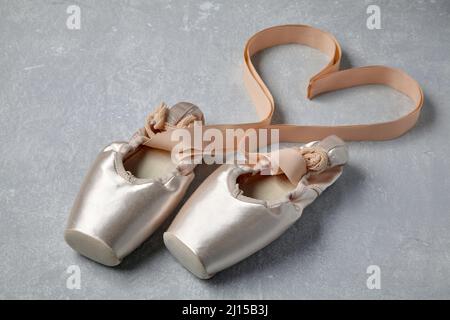 Beigefarbene spitzenschuhe mit Bändern, die in Herzform auf einem hellgrauen Betontisch angelegt sind. Ballettschuhe Stockfoto