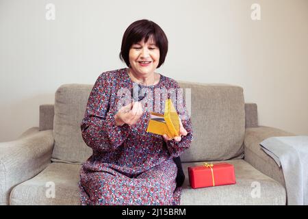 Oma öffnet ein Geschenk auf ihrem Sofa und wartet mit einem zweiten Geschenk Stockfoto